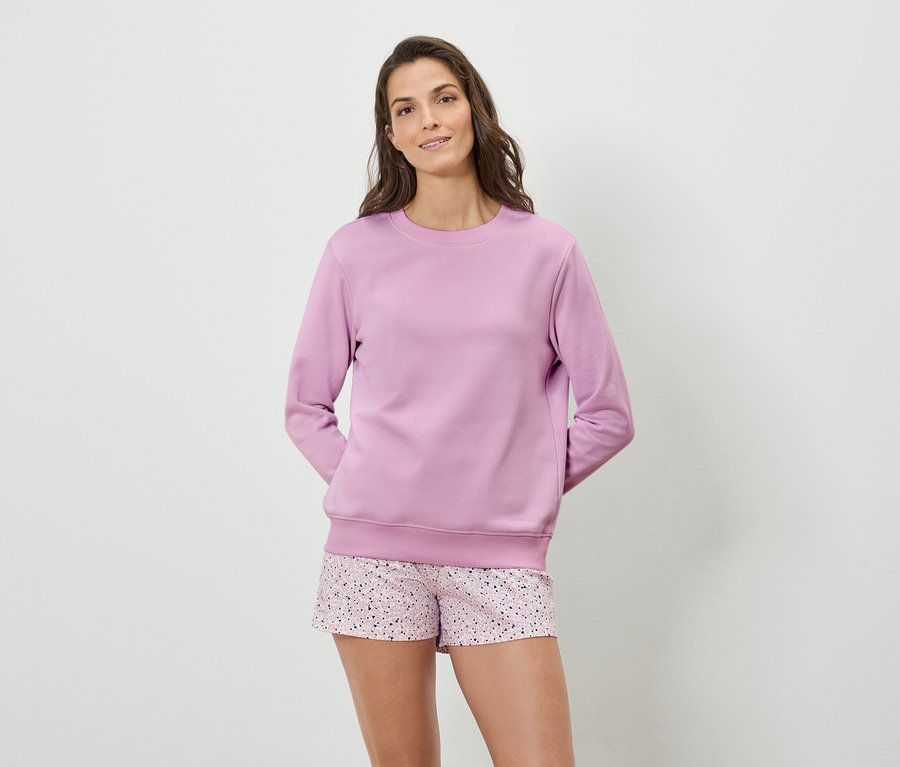 Frau trägt ein lila Sweatshirt und gemusterte Shorts.