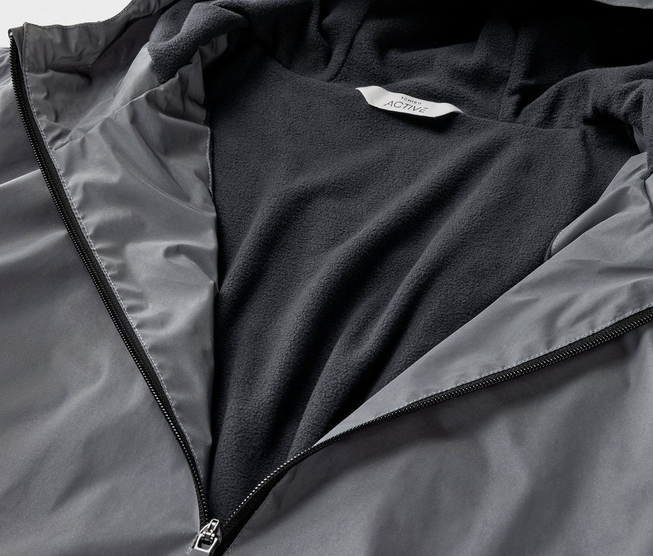 Detailaufnahme einer grauen, reflektierenden Sportjacke mit offenem Reißverschluss.