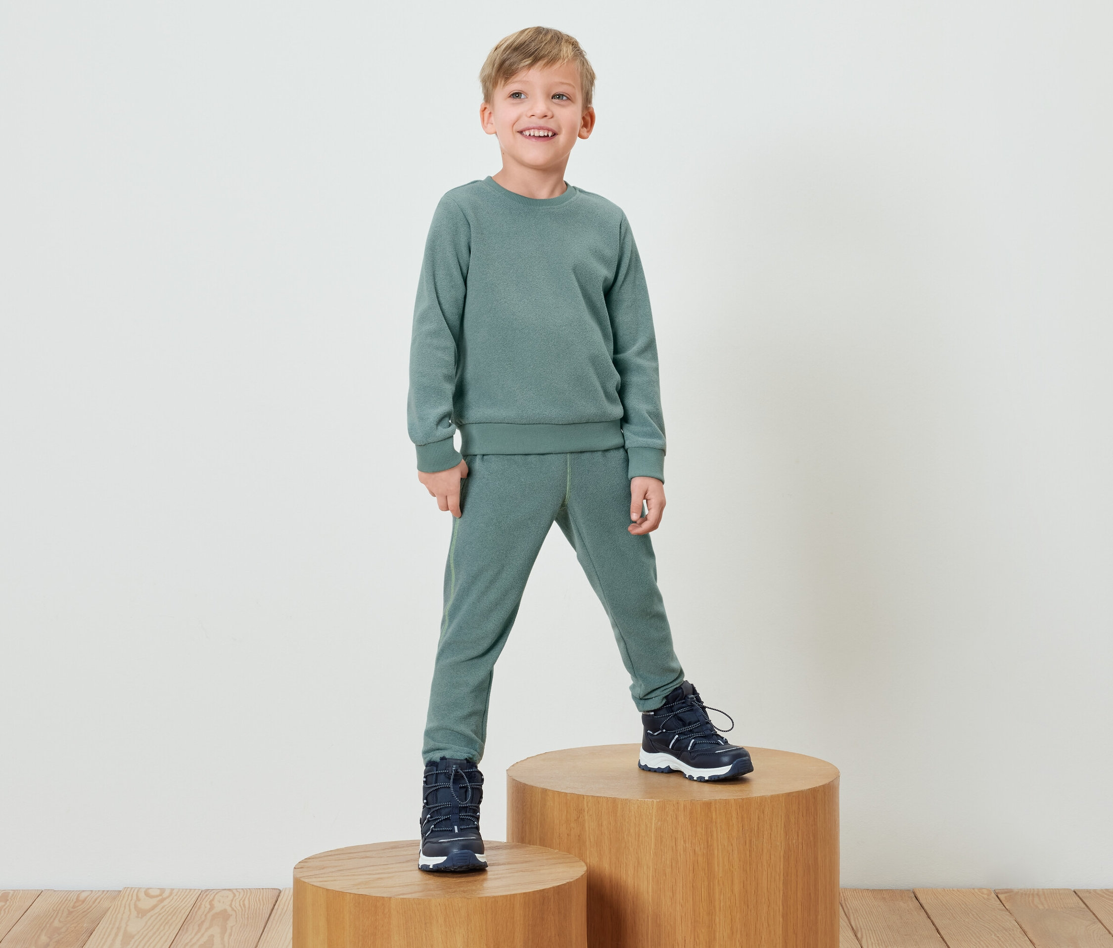 Ein Junge in einem grünen Trainingsanzug steht auf einem Holzsockel.