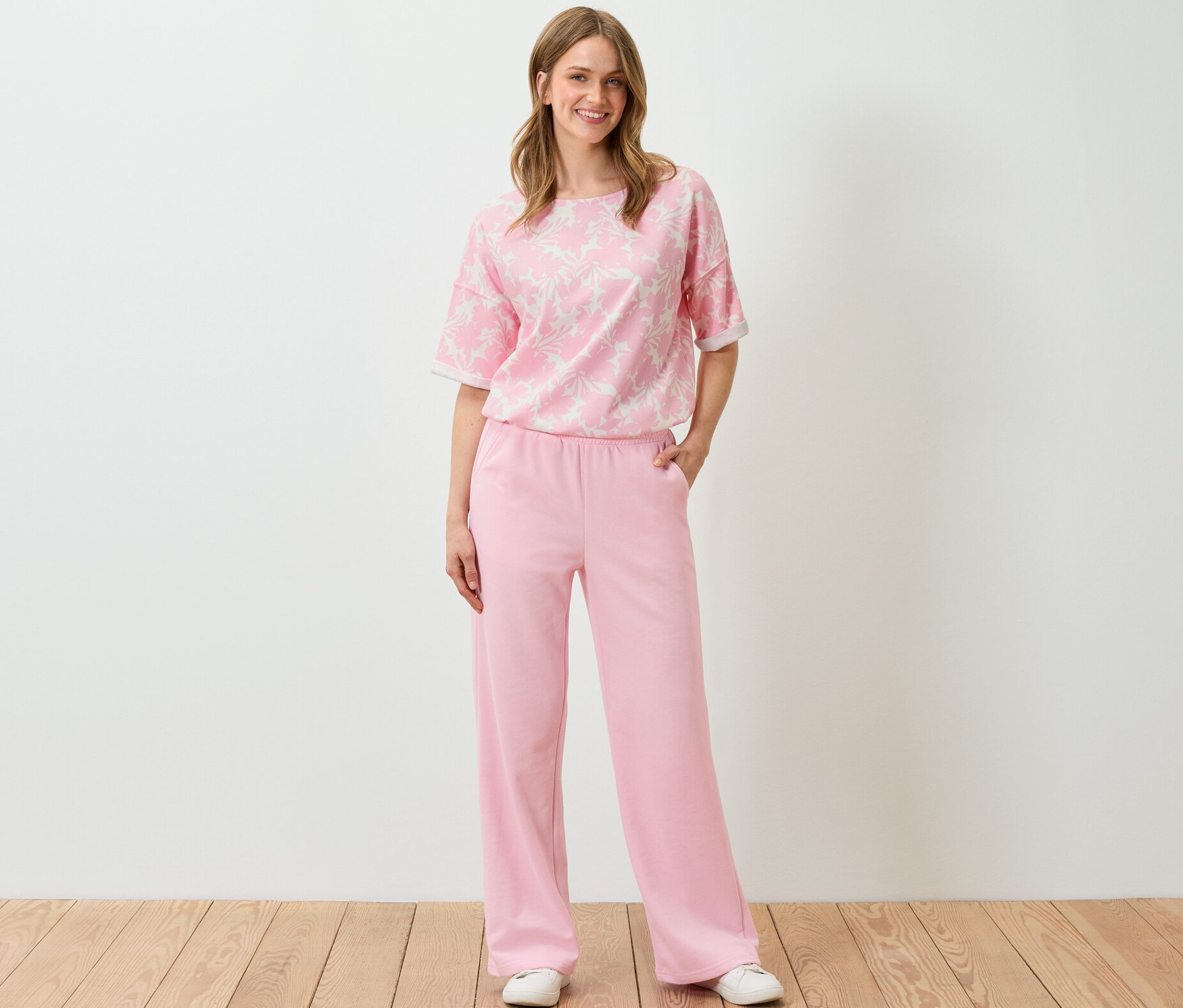 Frau steht und trägt ein roséfarbenes, bedrucktes Sweatshirt und eine Hose.