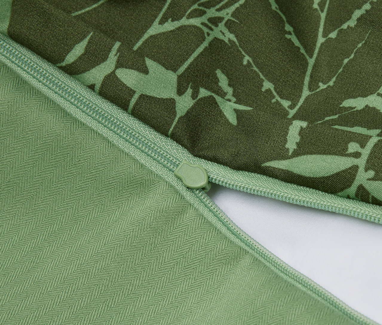 Detailansicht eines grünen Kissenbezugs mit Blumenmuster und Reißverschluss.