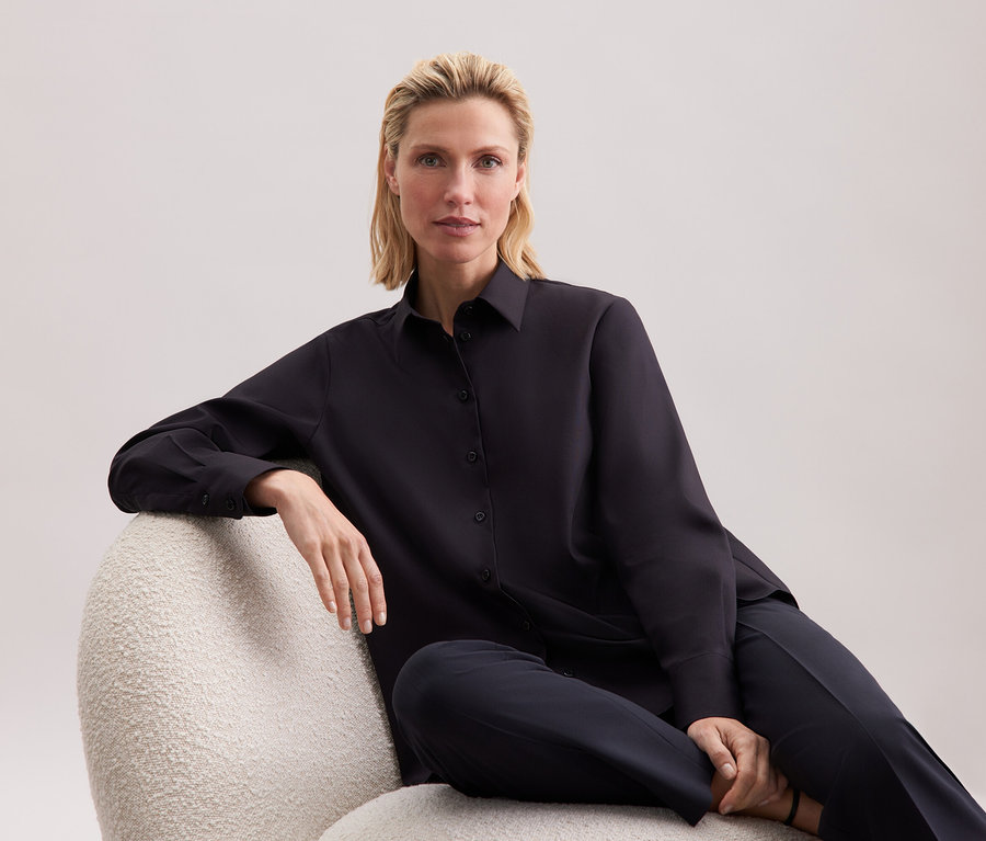 Blonde Frau sitzt in einem Sessel in schwarzem Hemd und Hose.