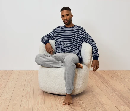 Mann sitzt in einem Sessel. Er trägt ein gestreiftes Langarmshirt und eine graue Jogginghose.