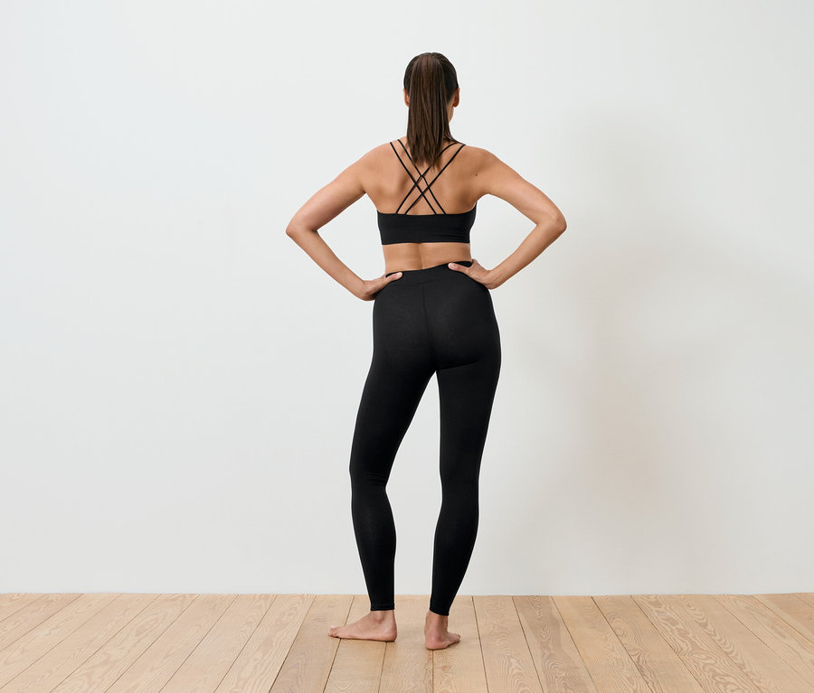 Frau mit dem Rücken zur Kamera in schwarzem Sport-BH und Leggings, die Hände in den Hüften.