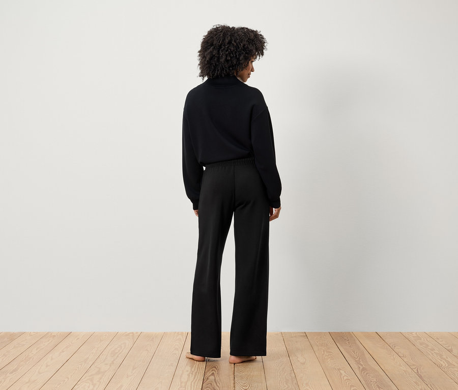 Eine Frau mit Afro-Frisur trägt einen schwarzen Pullover und eine schwarze Hose, von hinten gesehen.