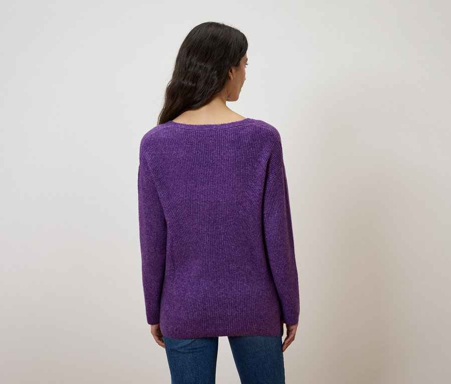Rückansicht einer Frau mit dunklem Haar, die einen lila Pullover und blaue Jeans trägt.