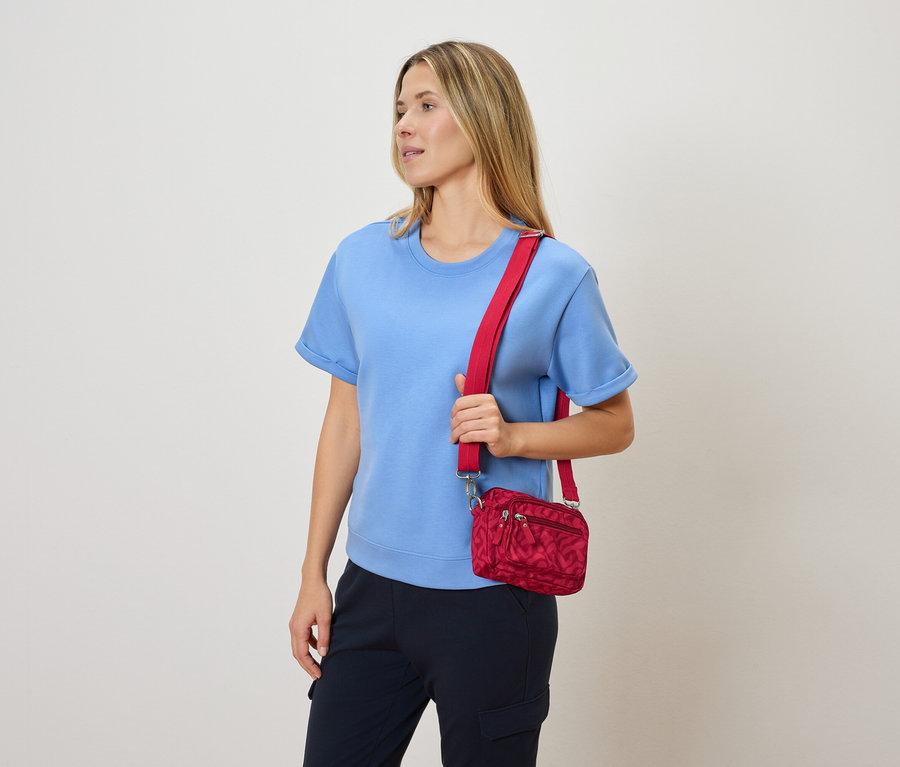 Frau mit blauer Bluse und marineblauer Hose, die eine rote Umhängetasche trägt.