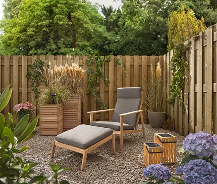 Ein Garten mit einem grauen Sessel und Hocker, zwei Bambus-Solar-Laternen und 5 LED-Solar-Spießen.