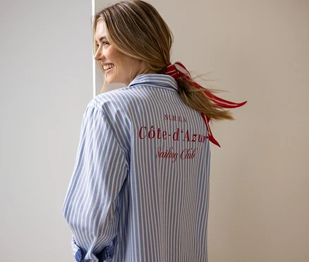 Frau trägt ein blau-weiß gestreiftes Hemd mit der Aufschrift "Sur la Côte-d'Azur Sailing Club" und ein rot-weiß gestreiftes Haarband.