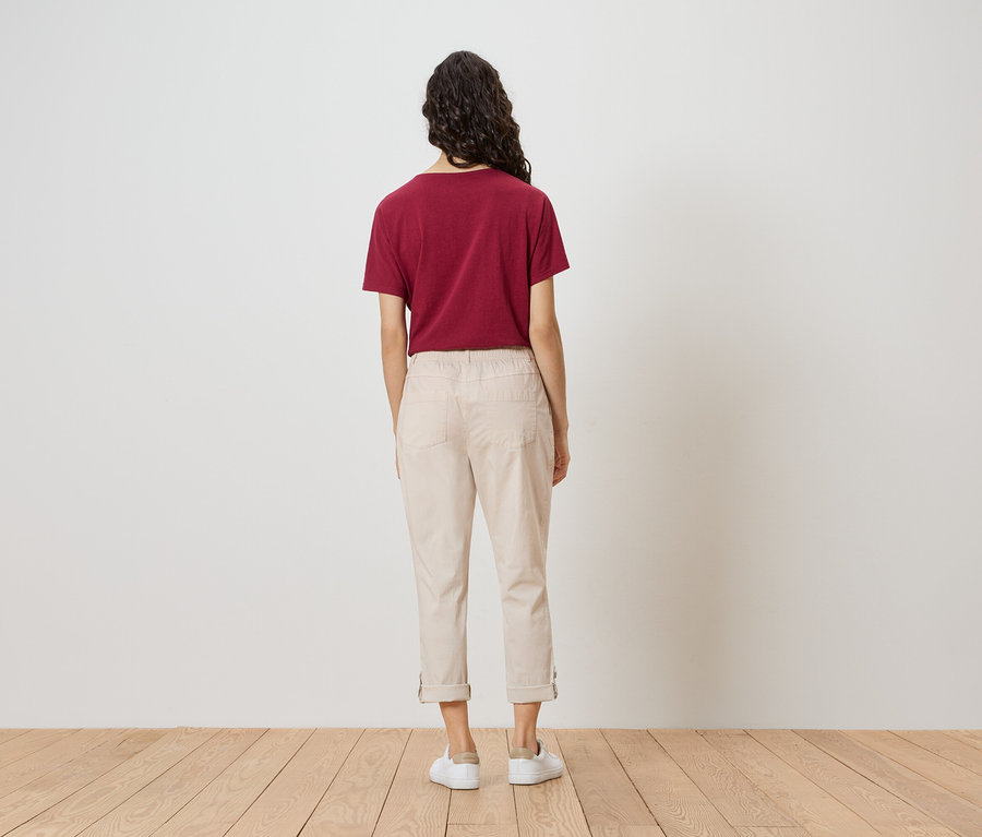 Eine Frau steht mit dem Rücken zur Kamera und trägt ein weinrotes T-Shirt, beigefarbene Hosen und weiße Schuhe.