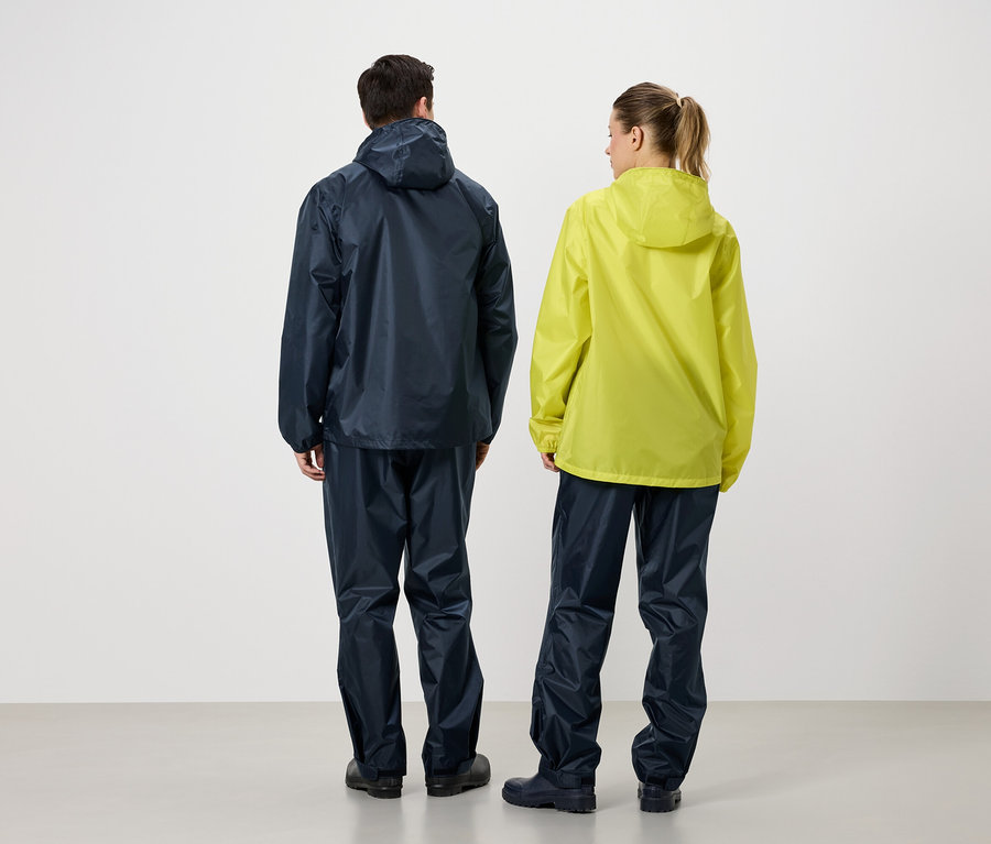 Rückansicht von zwei Personen, eine in marineblauer Regenjacke und Regenhose, die andere in gelber Regenjacke und marineblauer Regenhose.