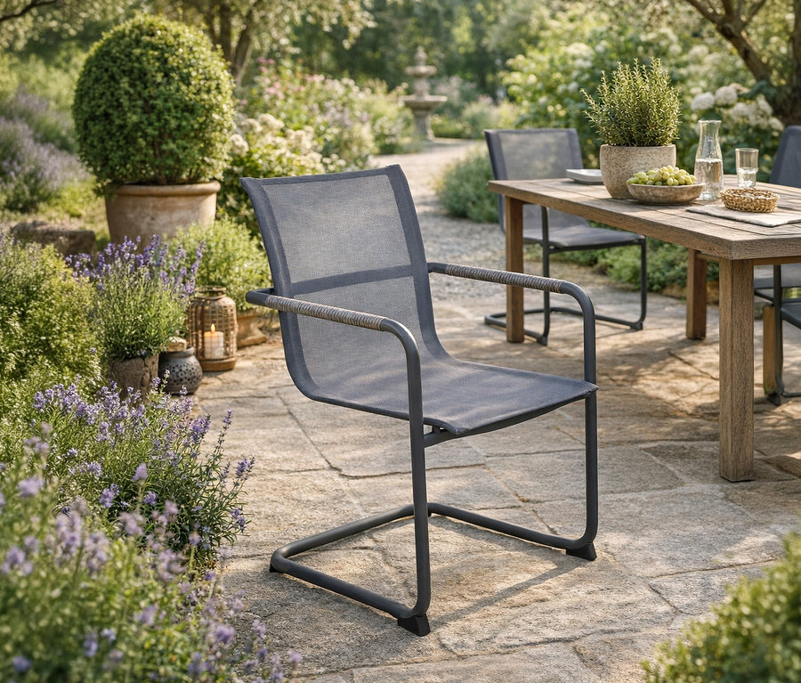 Ein grauer »Kendra« Freischwinger steht im Garten. Im Hintergrund ein Tisch mit zwei weiteren Stühlen.