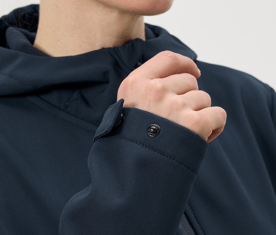 Nahaufnahme einer Person, die den Druckknopf am Ärmel einer marineblauen Jacke schliesst.