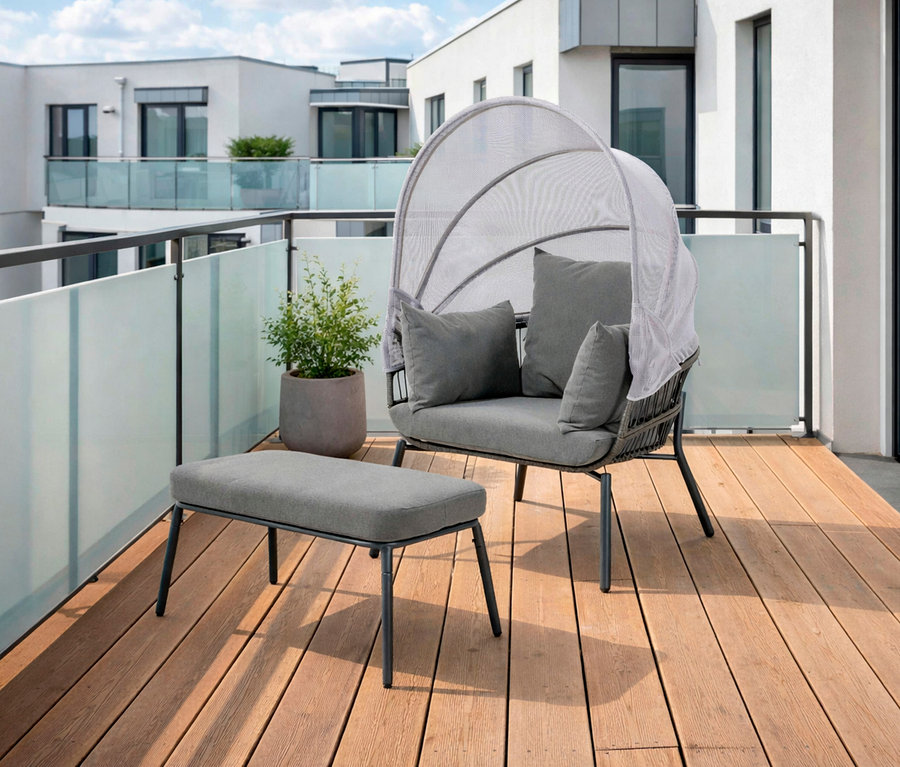 Auf einem Holzbalkon steht ein Leco Sessel mit Fußhocker, dazu ein Topf mit einer Pflanze vor einer Glasbrüstung.