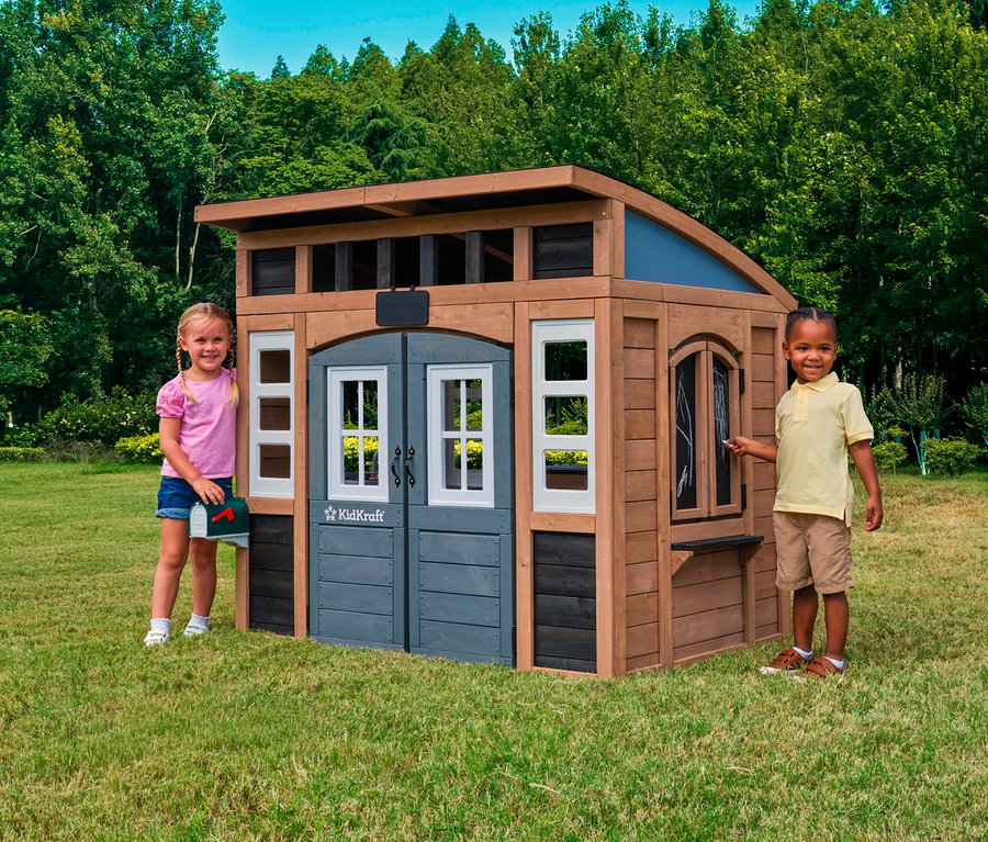 Zwei Kinder stehen vor dem Spielhaus Trolli auf einer Wiese. Ein Mädchen hält einen Briefkasten, ein Junge eine Kreide.