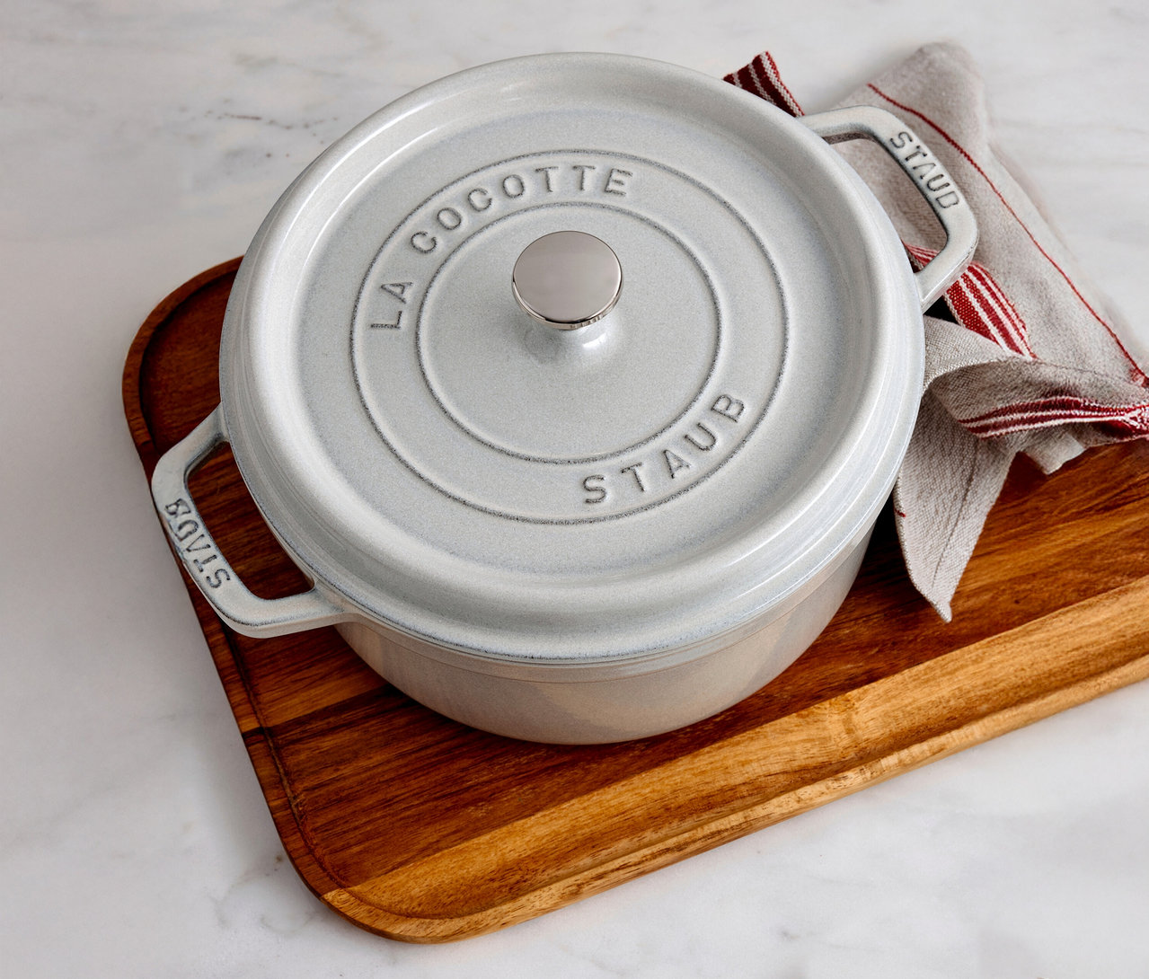 Ein weißer STAUB »Cocotte 24« Topf (ca. 3,7 l) steht auf einem Holzbrett neben einem Küchentuch.