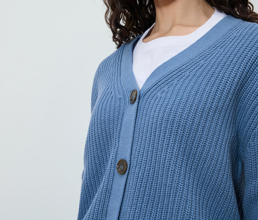 Eine Frau trägt eine blaue Strickjacke über einem weißen T-Shirt.