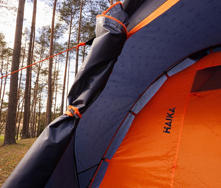 Blick ins Innere eines orangefarbenen Tambu »HAIKA 4« 4-Personen-Kuppelzelts auf einem Campingplatz.