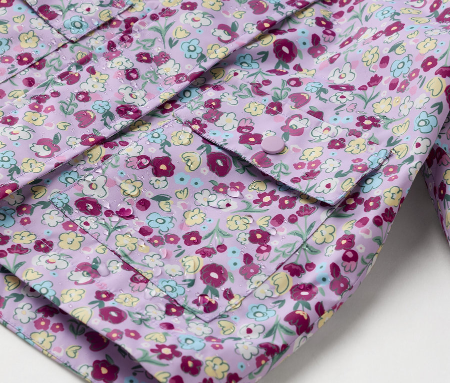 Nahaufnahme einer lila Regenjacke mit Blumenmuster und aufgesetzten Taschen, die mit Knöpfen geschlossen werden.
