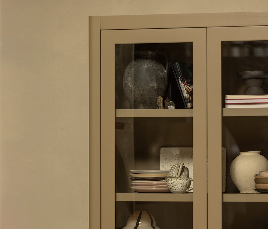 Ein beiger Schrank mit Glasböden zeigt eine Sammlung von Geschirr, Vasen und Dekorationsgegenständen.