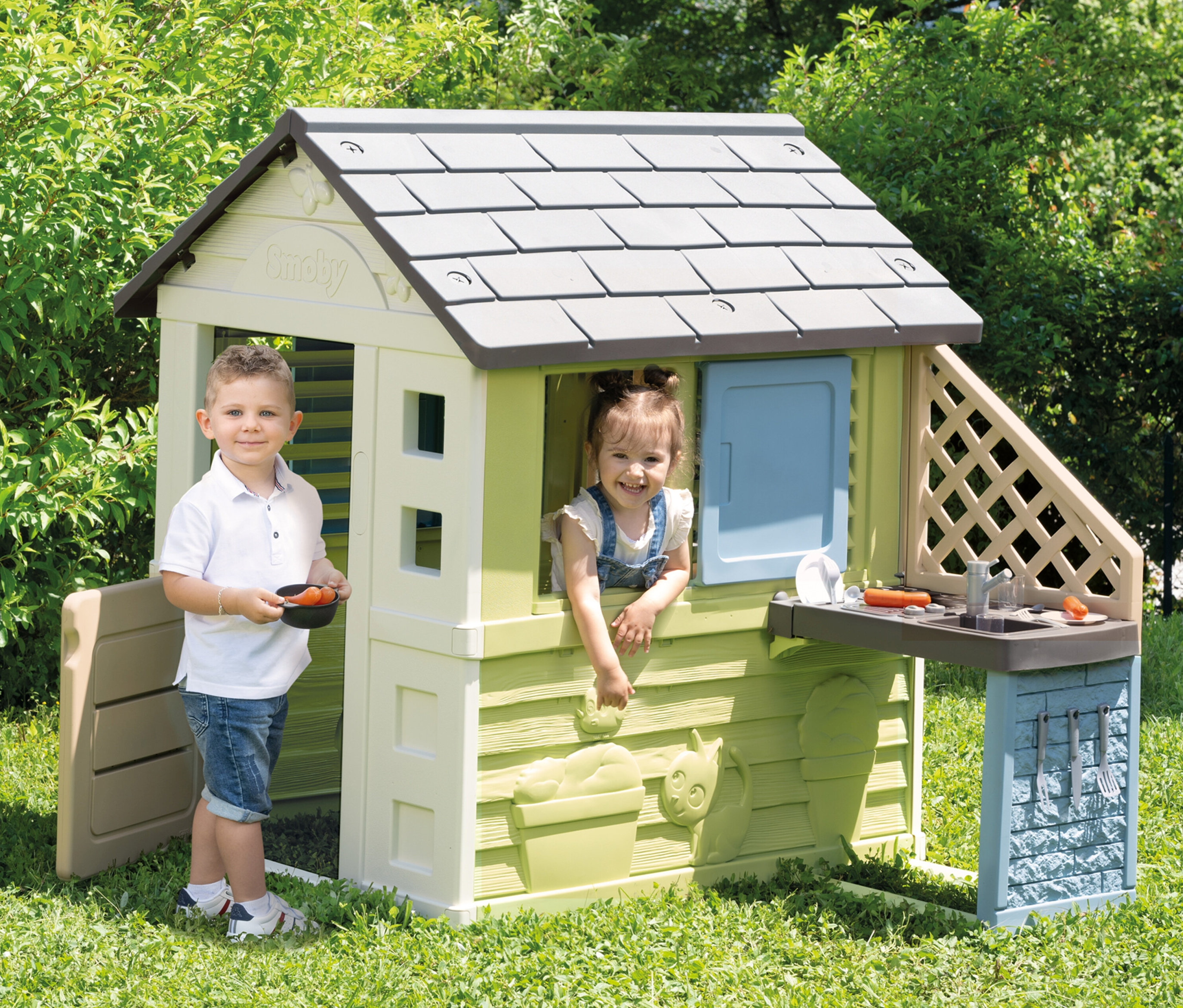 Junge mit Schale steht vor Smoby Life Spielhaus »Pretty« mit Küche, Mädchen lehnt aus Fenster.