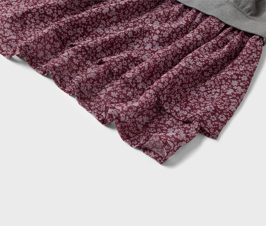 Nahaufnahme eines burgunderroten Stoffes mit kleinem Blumenmuster. Der Stoff ist gerafft und fällt in weichen Falten. Oben ist ein Stück gerippter, grauer Stoff zu sehen.