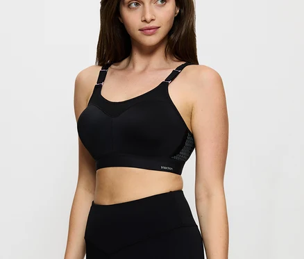 Frau trägt einen schwarzen TRIUMPH Minimizer-Sport-BH Triaction Control Lite W01X und schwarze Leggings, blickt nach rechts.
