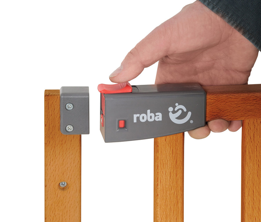 Eine Hand drückt den roten Knopf des grauen Verschlusses eines roba Treppenschutzgitters »Safety Up« aus Holz.