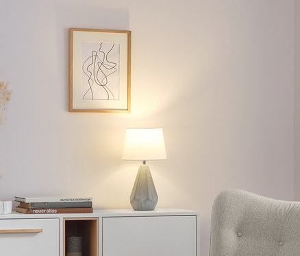 Tischleuchte mit Keramikfuß steht auf einer weißen Kommode im Wohnzimmer.