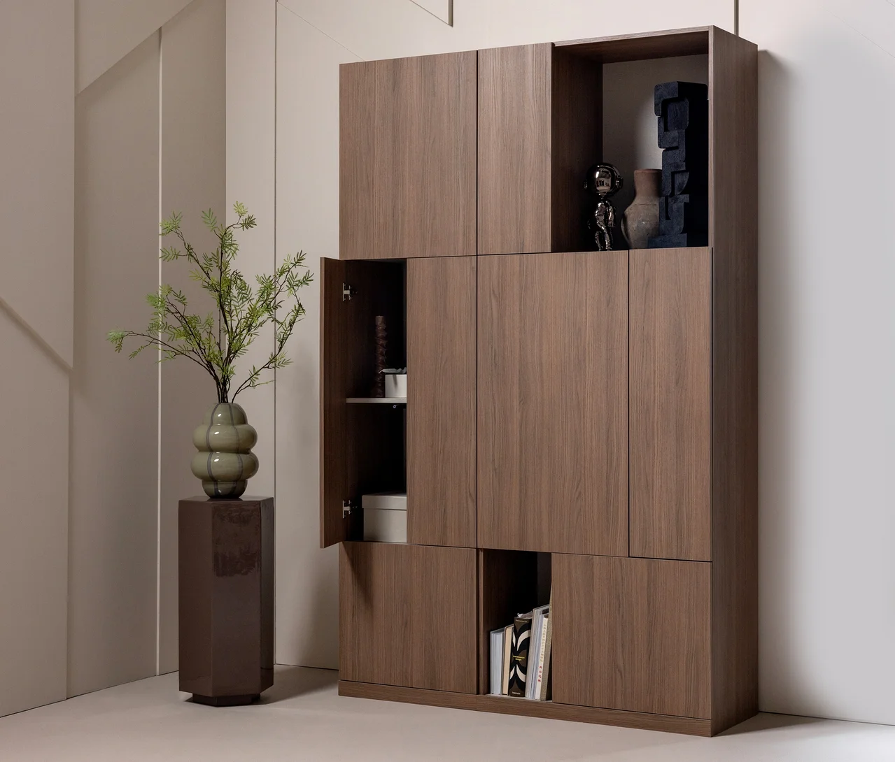 Dunkles Holz-Modulschranksystem mit geschlossenen Türen und offenen Regalen. Links steht ein hoher, dunkelbrauner Sockel mit einer grünen Vase und Zweigen. Offene Regale zeigen eine silberne Figur, eine dunkle Vase, eine schwarze Skulptur und Bücher.