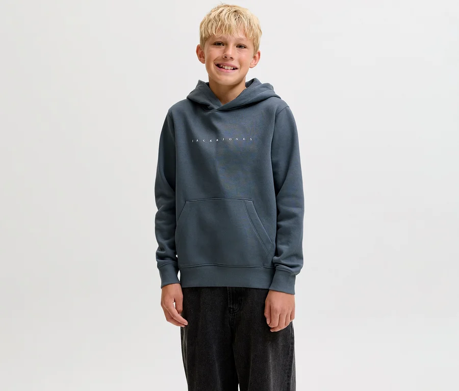 Lächelnder Junge trägt einen dunkelgrauen Jack&Jones Sweat-Hoodie Star mit Bauchtasche und dunkle Hose.