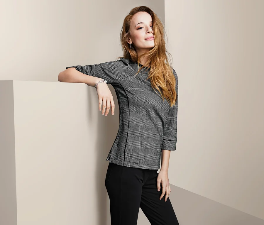 Frau posiert in einem Sweatshirt mit 3/4-Arm und einer schwarzen Hose.