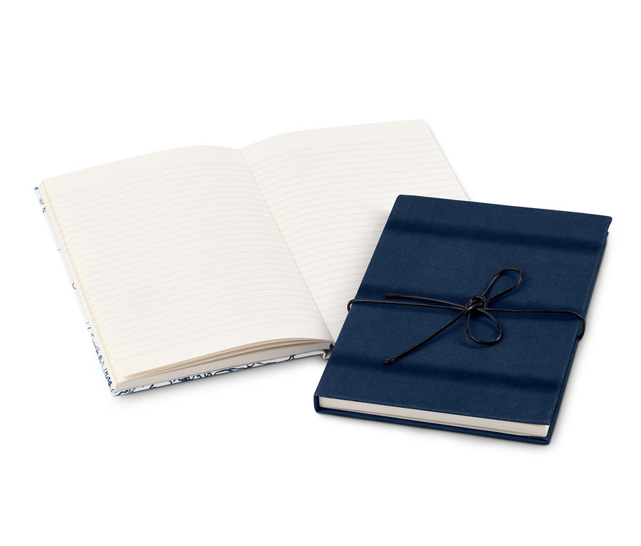 Zwei Notizbücher liegen auf einer weißen Oberfläche. Eines ist offen mit linierten Seiten, das andere ist geschlossen, mit dunkelblauem Papier umwickelt und mit einer schwarzen Schnur verschnürt.