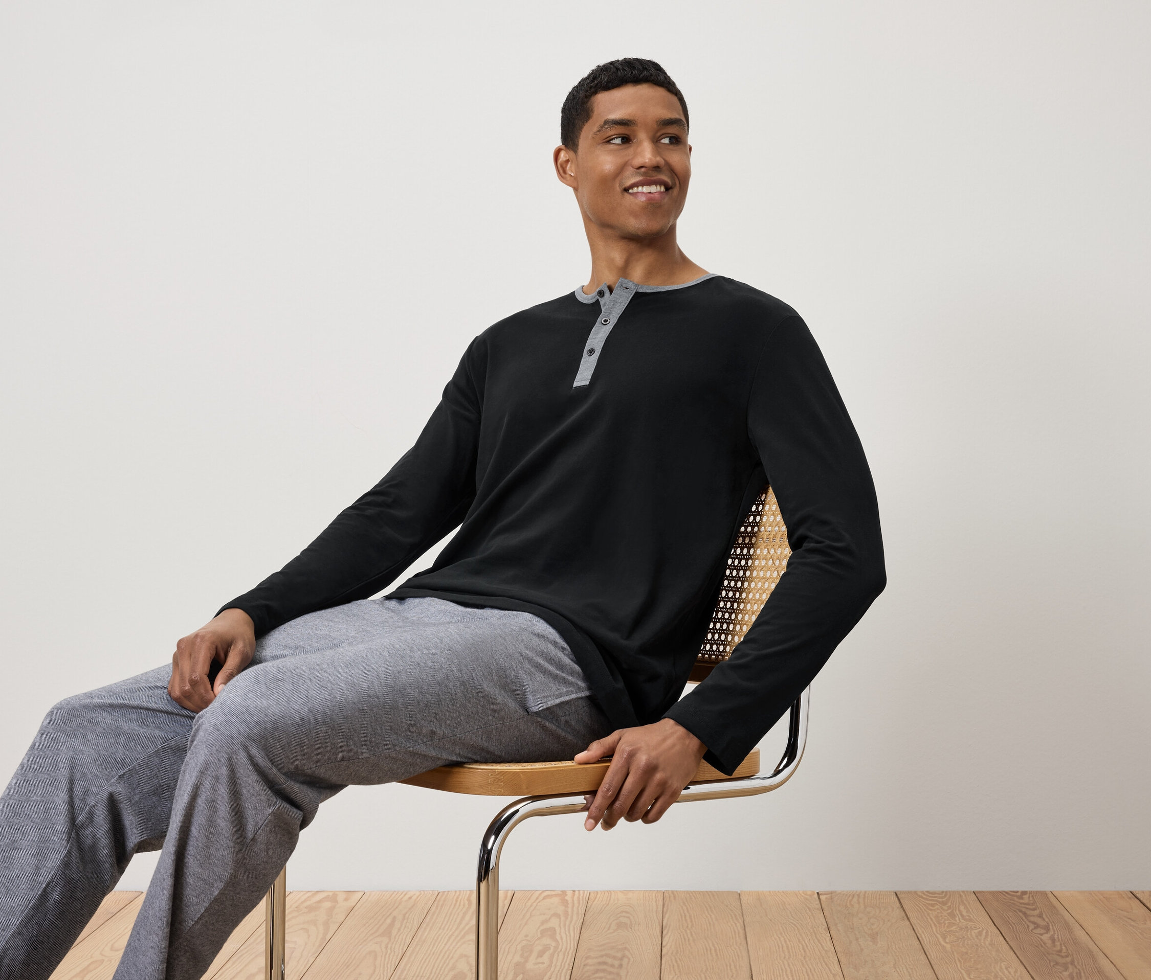 Mann sitzt auf einem Stuhl, trägt ein schwarzes Langarmshirt und graue Trainingshose.