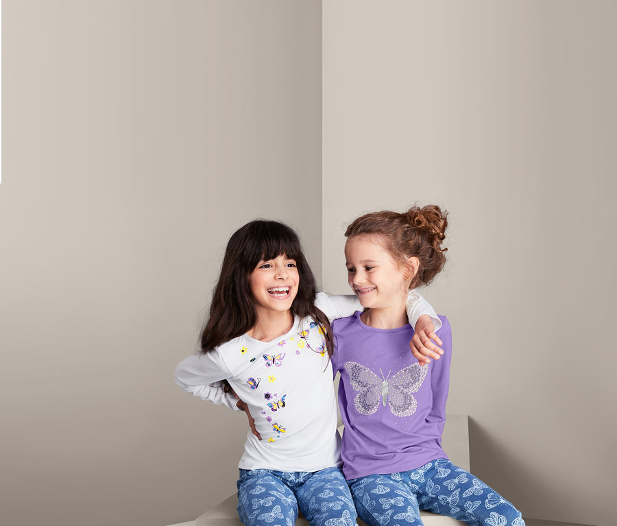 Mädchen sitzen in 2 Langarmshirts mit Schmetterlingen.