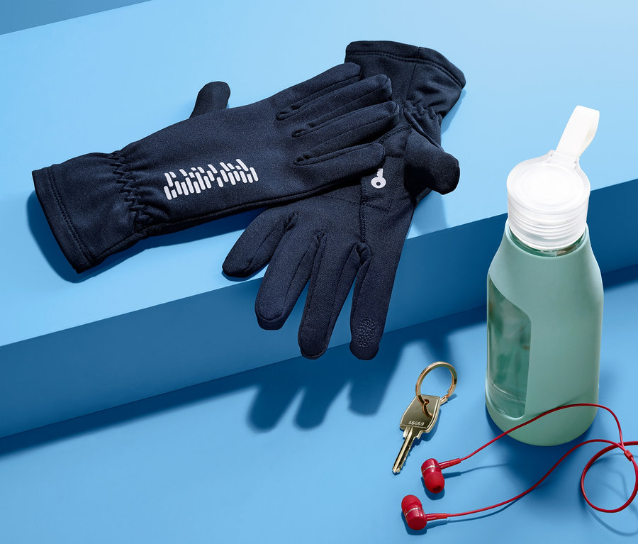 Schwarze Laufhandschuhe liegen neben einer grünen Wasserflasche, Schlüsseln und roten Kopfhörern auf blauem Hintergrund.