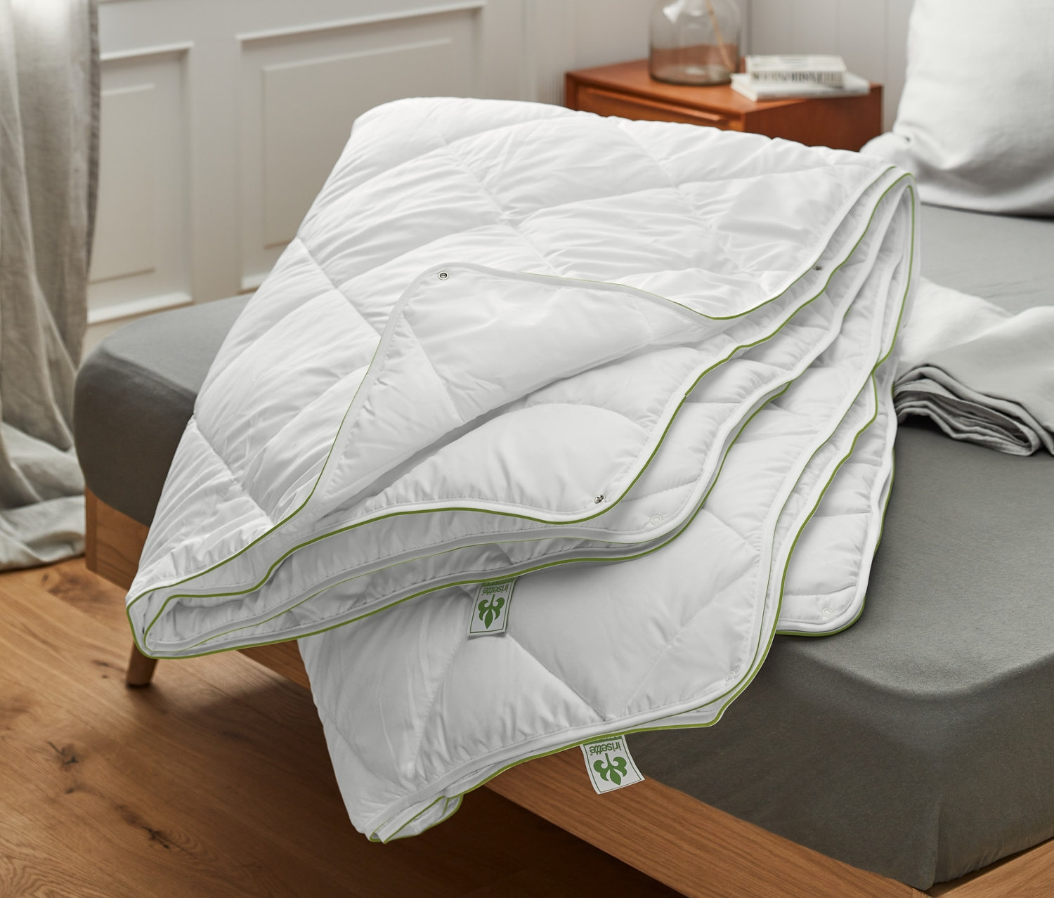 Ein gefaltetes irisette® greenline 4-Jahreszeiten-Steppbett liegt auf einem Bett.