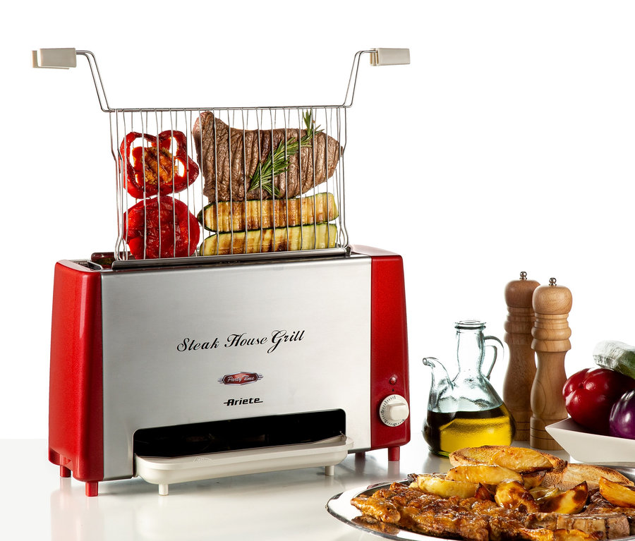 Auf einem Tisch steht ein Ariete Vertical Steakhouse 730 Grill mit Fleisch, Paprika und Zucchini im Gitter. Neben dem Grill befinden sich ein Teller mit Fleisch und Kartoffeln, Olivenöl und Gemüse.