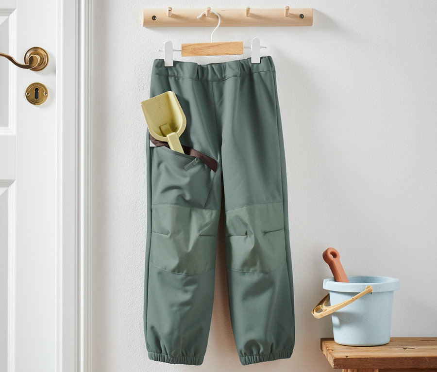 Eine Softshell-Hose hängt mit Spielzeug in der Tasche und daneben auf einem Hocker.