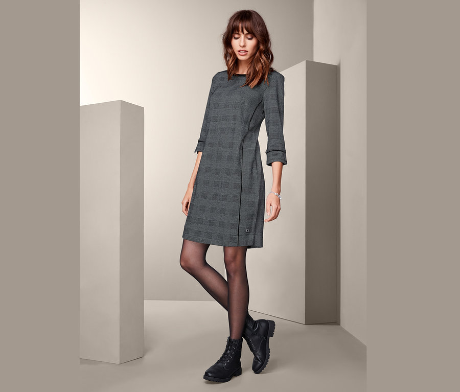 Frau posiert in einem Sweatkleid mit 3/4-Arm und schwarzen Stiefeln.