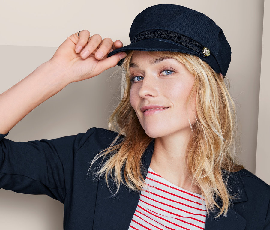 Frau richtet ihre Schiffermütze. Sie trägt einen blauen Blazer und ein rot-weiß gestreiftes T-Shirt.