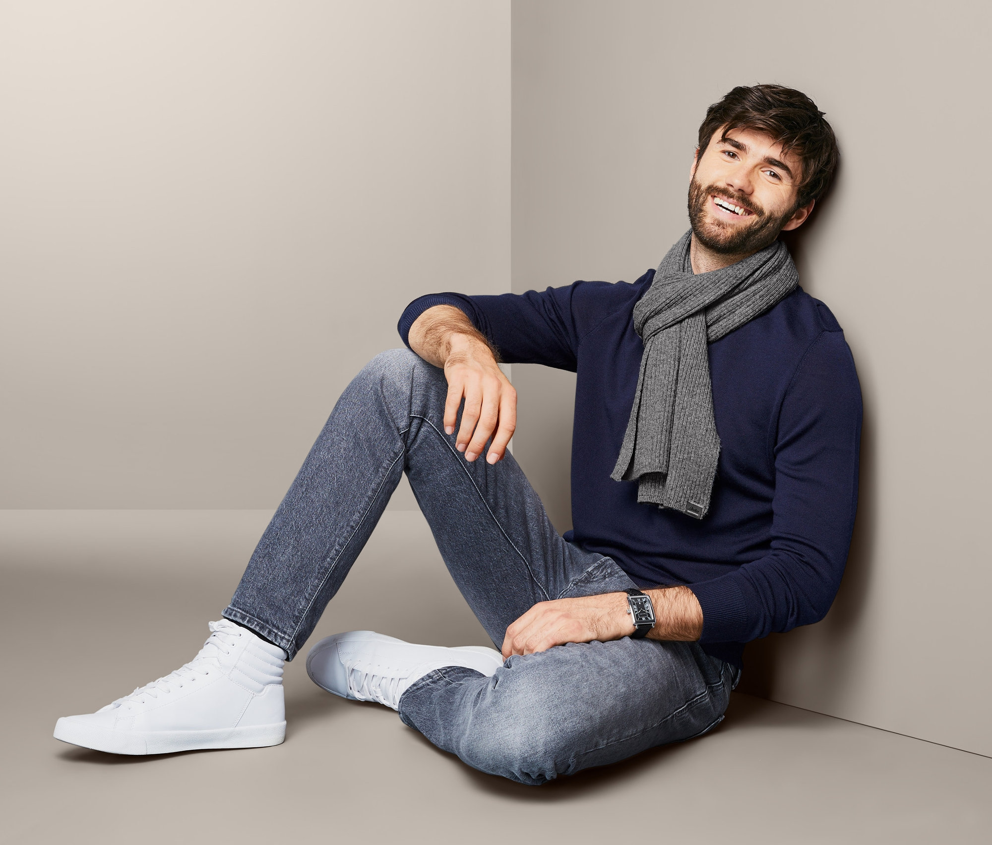 Mann sitzt an eine Wand gelehnt und trägt einen Strickschal.