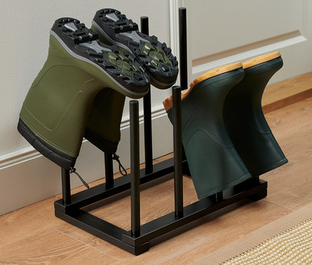 Zwei Paar grüne Gummistiefel stehen auf einem schwarzen Stiefelhalter.
