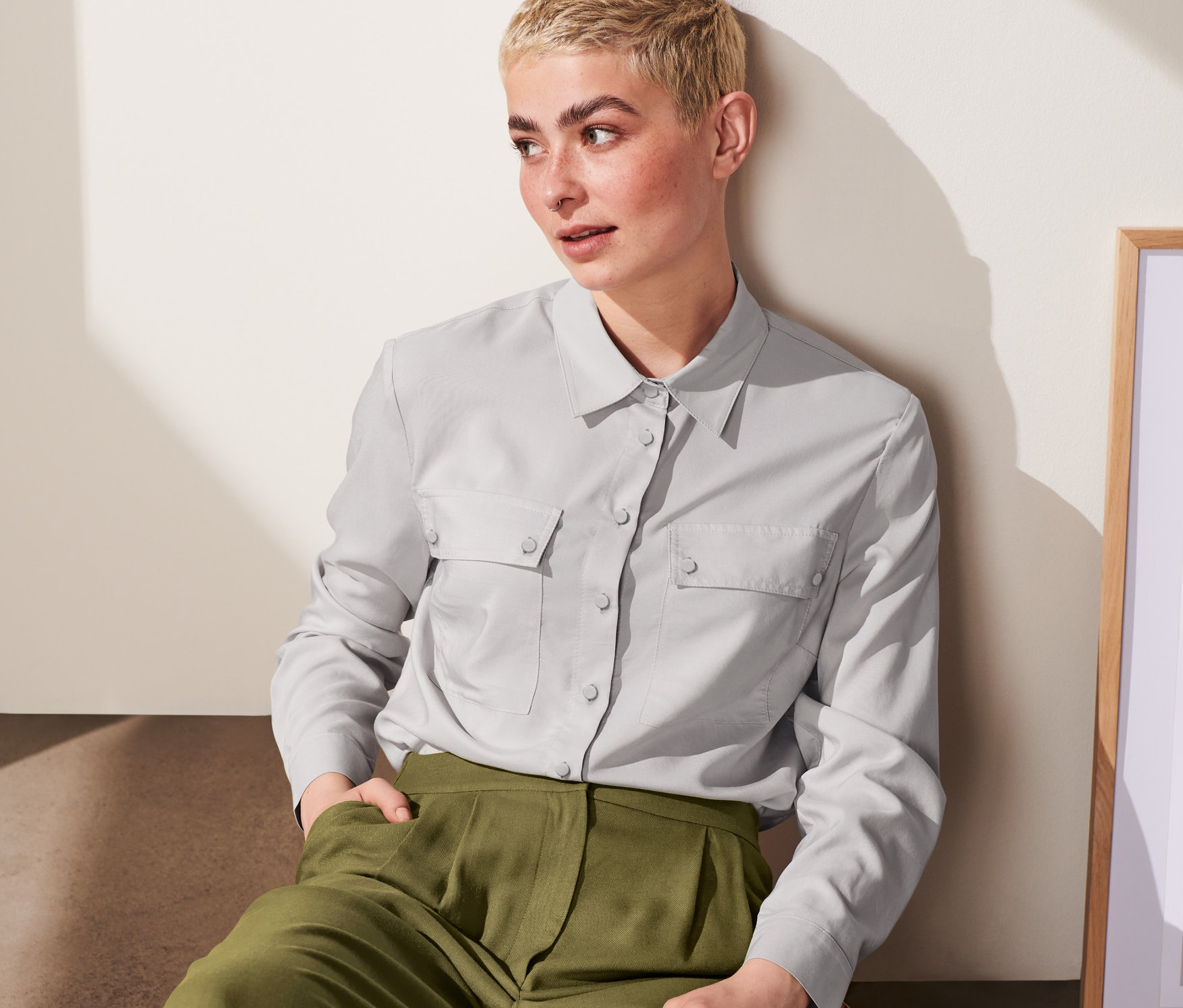 Frau sitzt und trägt eine hellgraue Hemdbluse.