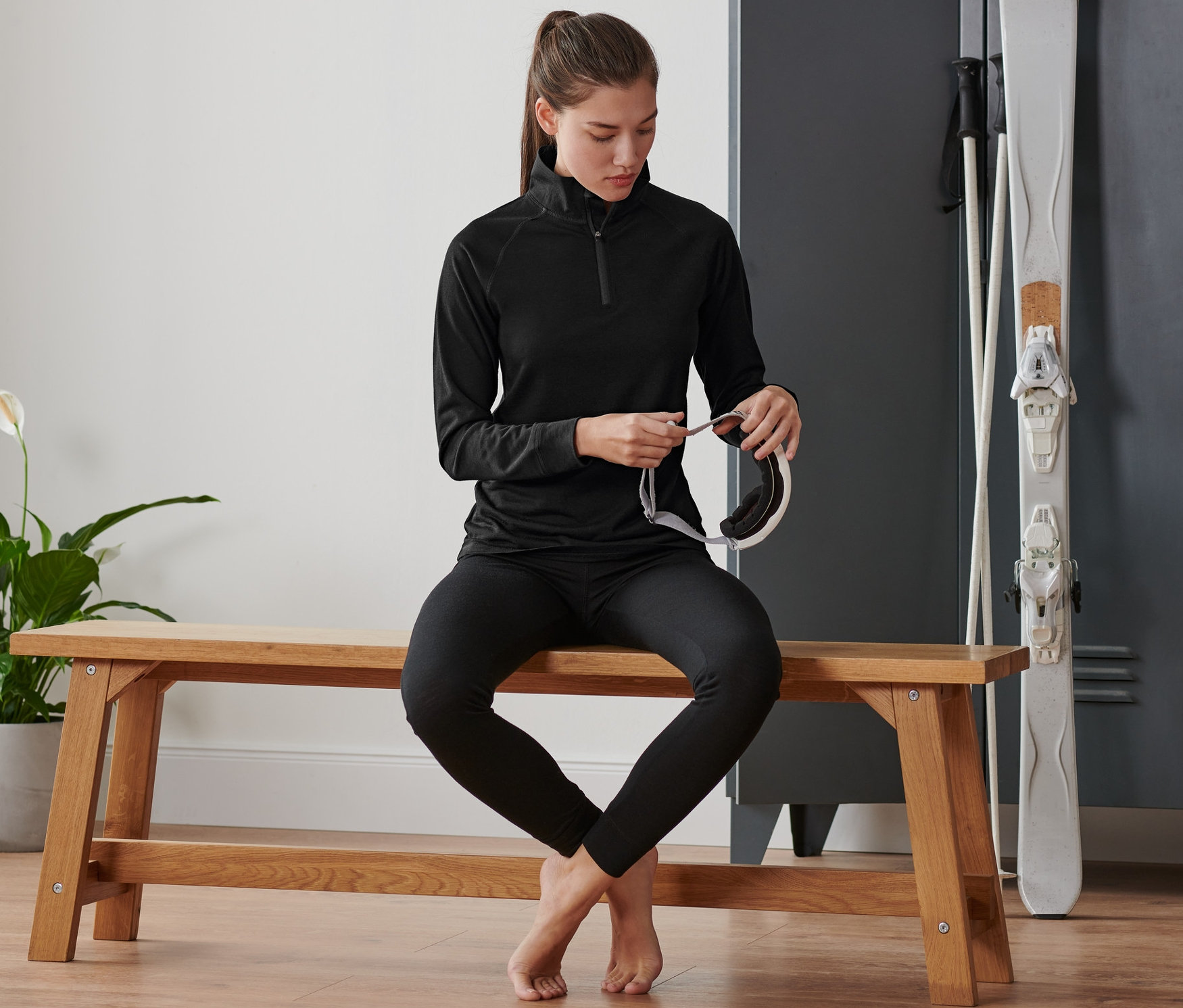 Frau sitzt auf einer Bank und hält eine Skibrille. Sie trägt ein Funktionsshirt mit Merinowolle.