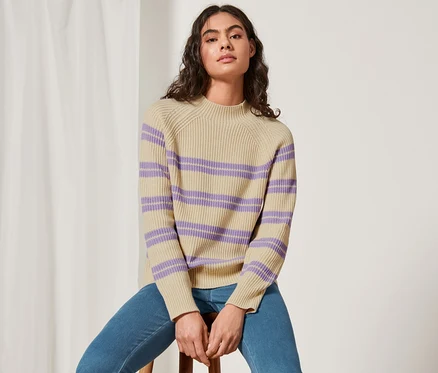 Frau sitzt auf einem Hocker und trägt einen gestreiften Strickpullover.