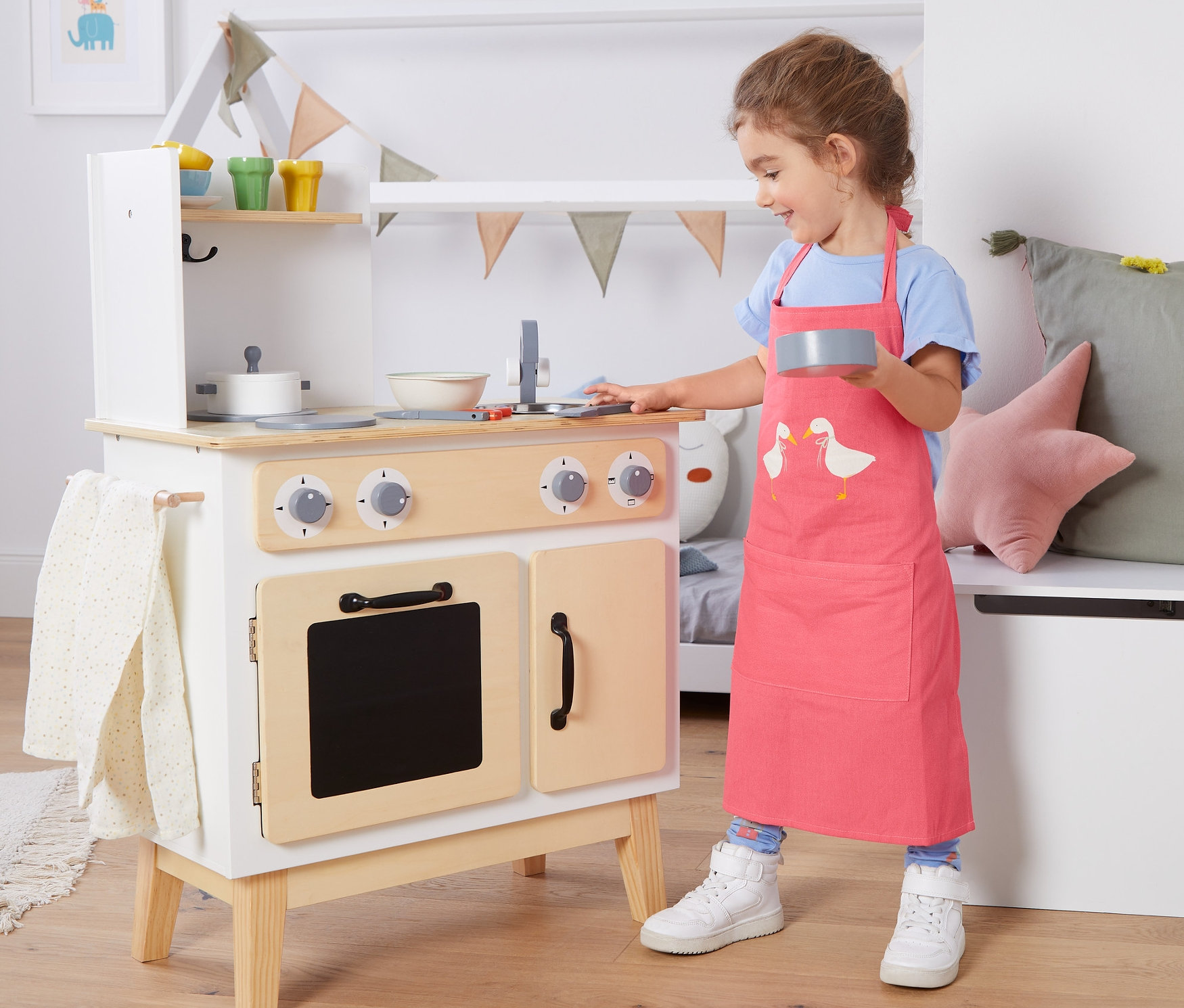 Mädchen spielt mit Spielküche und trägt eine Kinder-Küchenschürze.