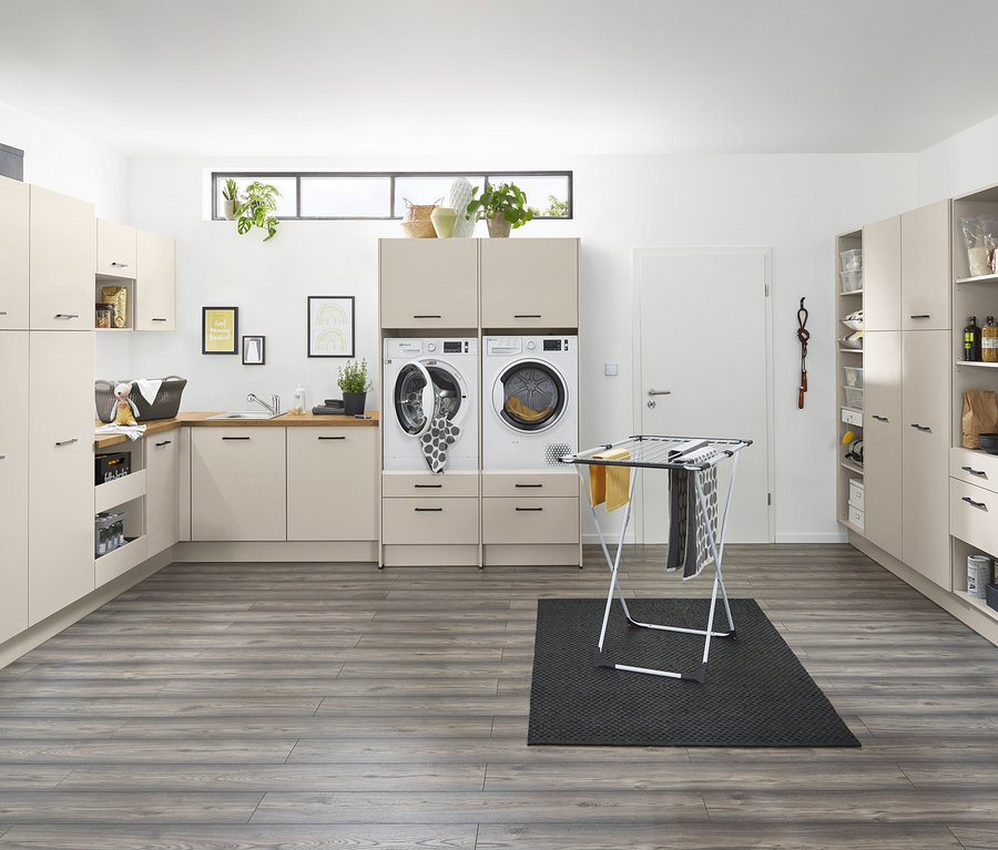 Funktionaler Waschraum mit Waschmaschine, Trockner und Schränken in neutralen Tönen. Ein Wäscheständer steht auf einem dunklen Teppich. In der linken Ecke befindet sich ein Unterschrankmodul mit Abfallsammler, links, kieselgrau.
