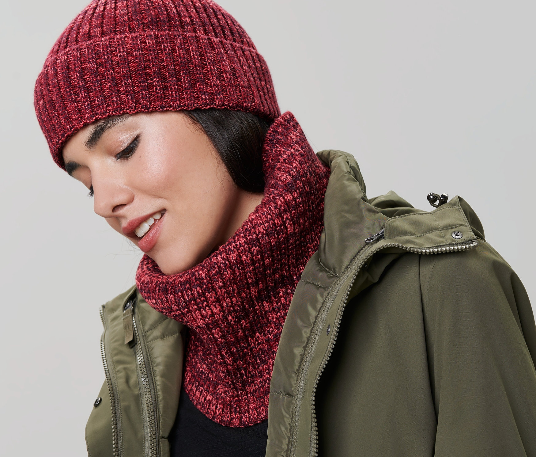 Frau trägt einen Strickschlauchschal und eine Mütze. Sie trägt eine grüne Jacke.