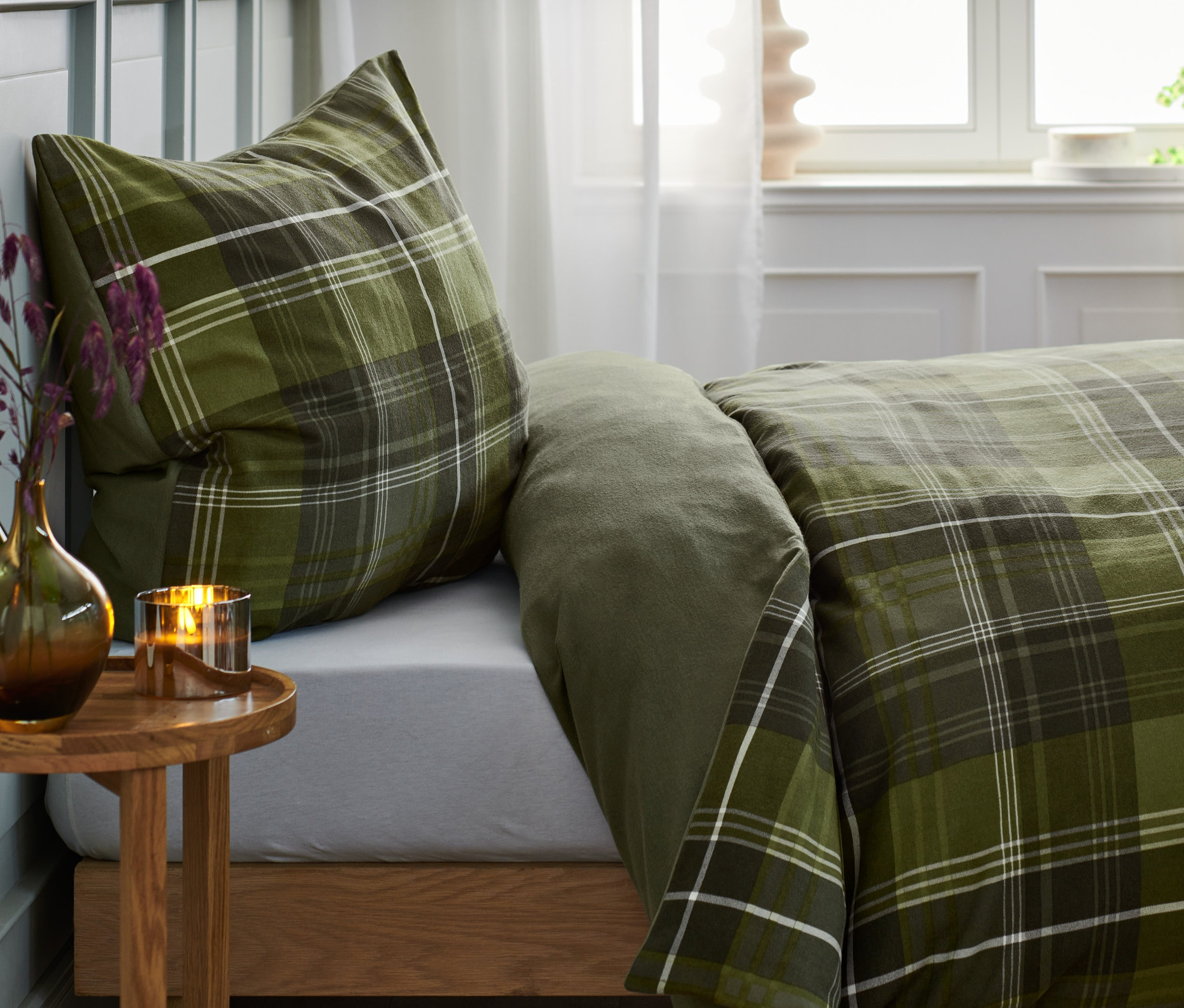 Grün karierte Flanell-Bettwäsche auf einem Bett mit Nachttisch.